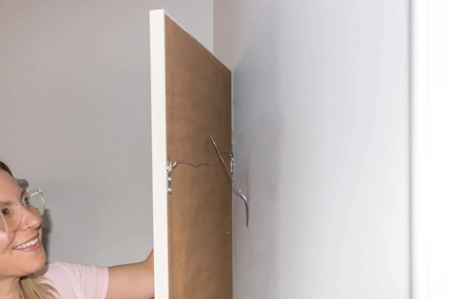 A view behind a white picture frame showing the picture wire successfully engaged on the wall nail after being guided into place with the fork.